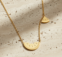 Gold necklace with watermelon slice pendants on a textured beige surface