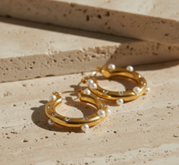 Gold hoop earrings with pearls on a beige stone surface